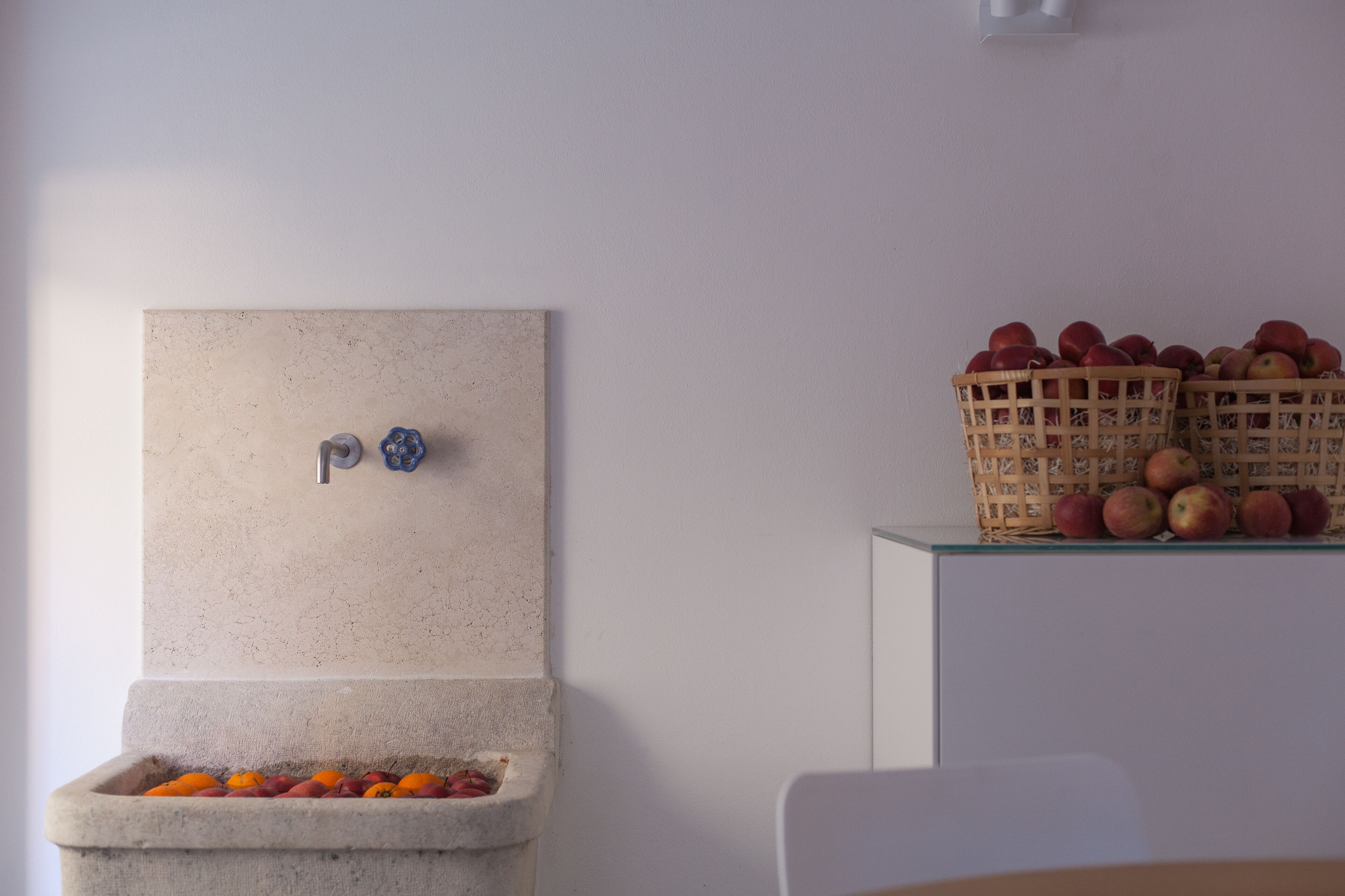 Un baño con un lavabo de piedra, una llave y un espejo montado en la pared. Hay cestas de manzanas en un estante sobre el lavabo.