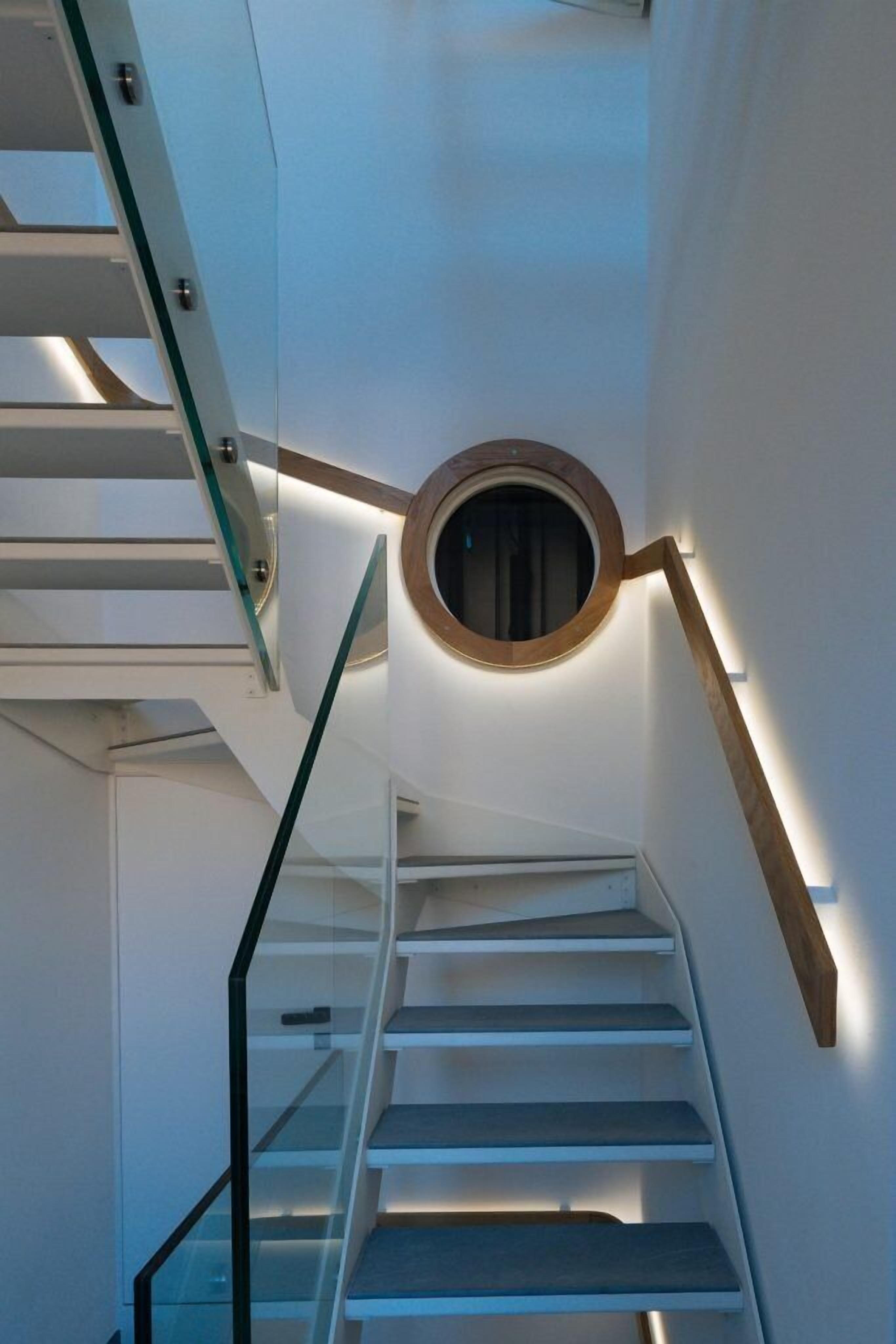 A modern staircase with glass railings and a circular window at the top.