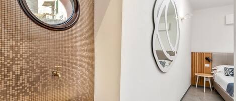 A bathroom with a mosaic tile wall, a round mirror, a sink, and a bed with a wooden headboard.