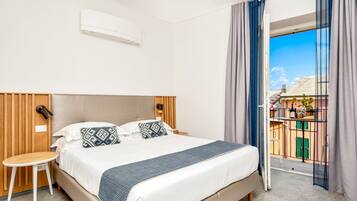 Ein Hotelzimmer mit einem Bett, Nachttischen, einem Fenster mit Vorhängen und einer Klimaanlage.