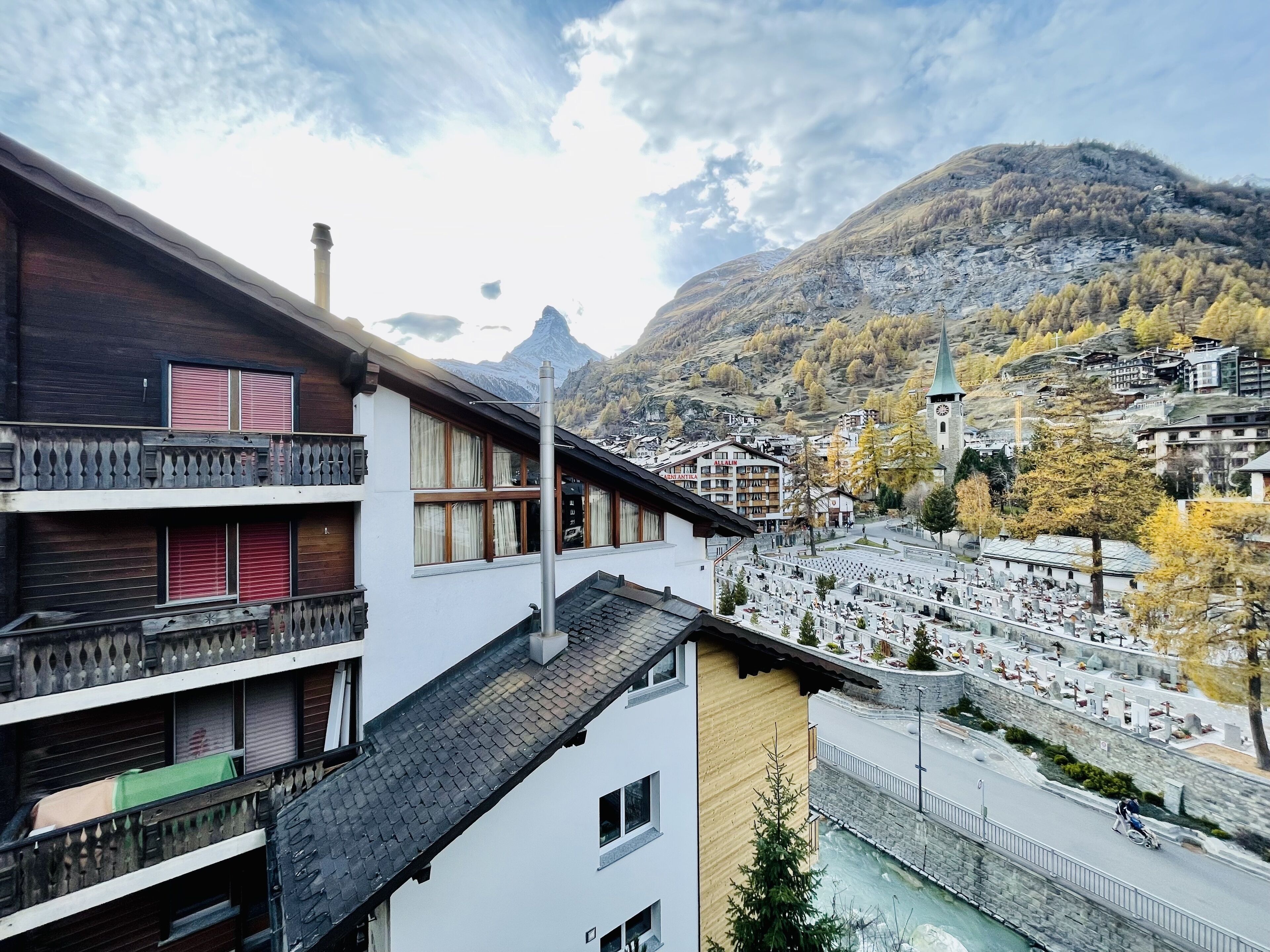 A multi-story building with balconies, a ski resort area, and a mountain backdrop.
