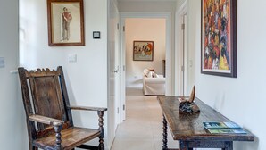Un pasillo con una silla de madera, una mesa con una escultura de cuerno y varias obras de arte enmarcadas en las paredes.