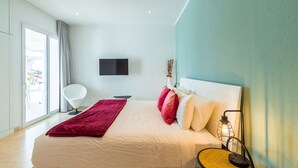 Quarto de hotel moderno com uma cama grande, televisão de tela plana na parede e uma janela ampla com vista para o exterior.