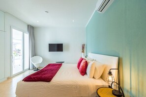 A modern hotel room with a large bed, a flat-screen TV mounted on the wall, and a large window providing a view of the outside. - Perfect for Groups! 7BR Villa w/ Pool, Ocean Views (Noord)