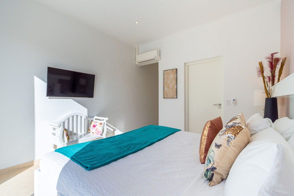 Habitación de hotel con cama, televisor, aire acondicionado, puerta y una obra de arte colgada en la pared.