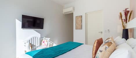 Habitación de hotel con cama, televisor, aire acondicionado, puerta y una obra de arte colgada en la pared.