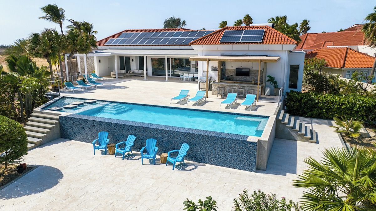 Una casa moderna con piscina, sillones de baño de sol y una zona de patio cubierta.