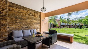 Un área de estar moderna al aire libre con un muro de ladrillo, mobiliario de mimbre y vistas a un césped cuidado y edificios.