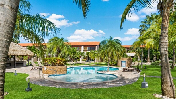 Una piscina rodeada de palmeras y sillas de descanso, con un edificio al fondo.