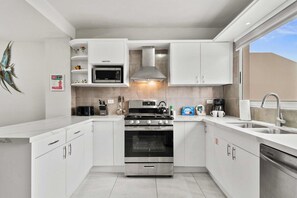 Une cuisine moderne avec des meubles blancs, des appareils en acier inoxydable et un four à micro-ondes encastré.