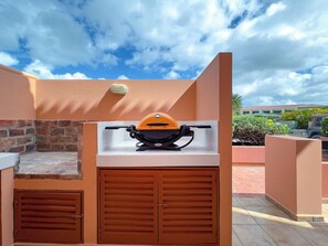 Un barbecue extérieur installé contre un mur, avec une base en briques et un plan de travail blanc au-dessus.