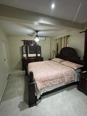 A bedroom with a bed, a nightstand, a dresser, a ceiling fan, and a window with curtains.