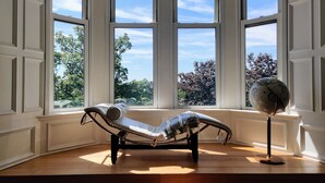Een kamer met een chaise longue bij grote ramen, een wereldbol op een standaard en een houten vloer.