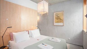 Ein modernes Hotelzimmer mit einem Bett, Nachttischlampen, einem gerahmten Kunstwerk an der Wand und ordentlich gefalteten Handtüchern auf dem Bett.
