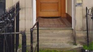 A wooden front door with a glass panel, a small step leading up to it, and a black metal gate to the left. - Very central, next to the Castle with garden (Edinburgh)