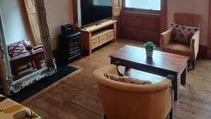 A living room with a large mirror, a television, a wooden coffee table, a sofa, and a chair. - Very central, next to the Castle with garden (Edinburgh)