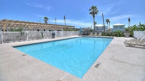 Piscina rectangular con agua azul cristalina, rodeada por una valla blanca y sillas de descanso.