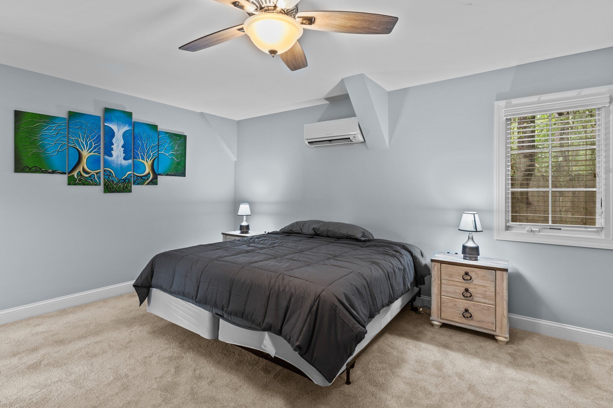 Une chambre à coucher avec un lit, une table de chevet, un ventilateur de plafond et une fenêtre.