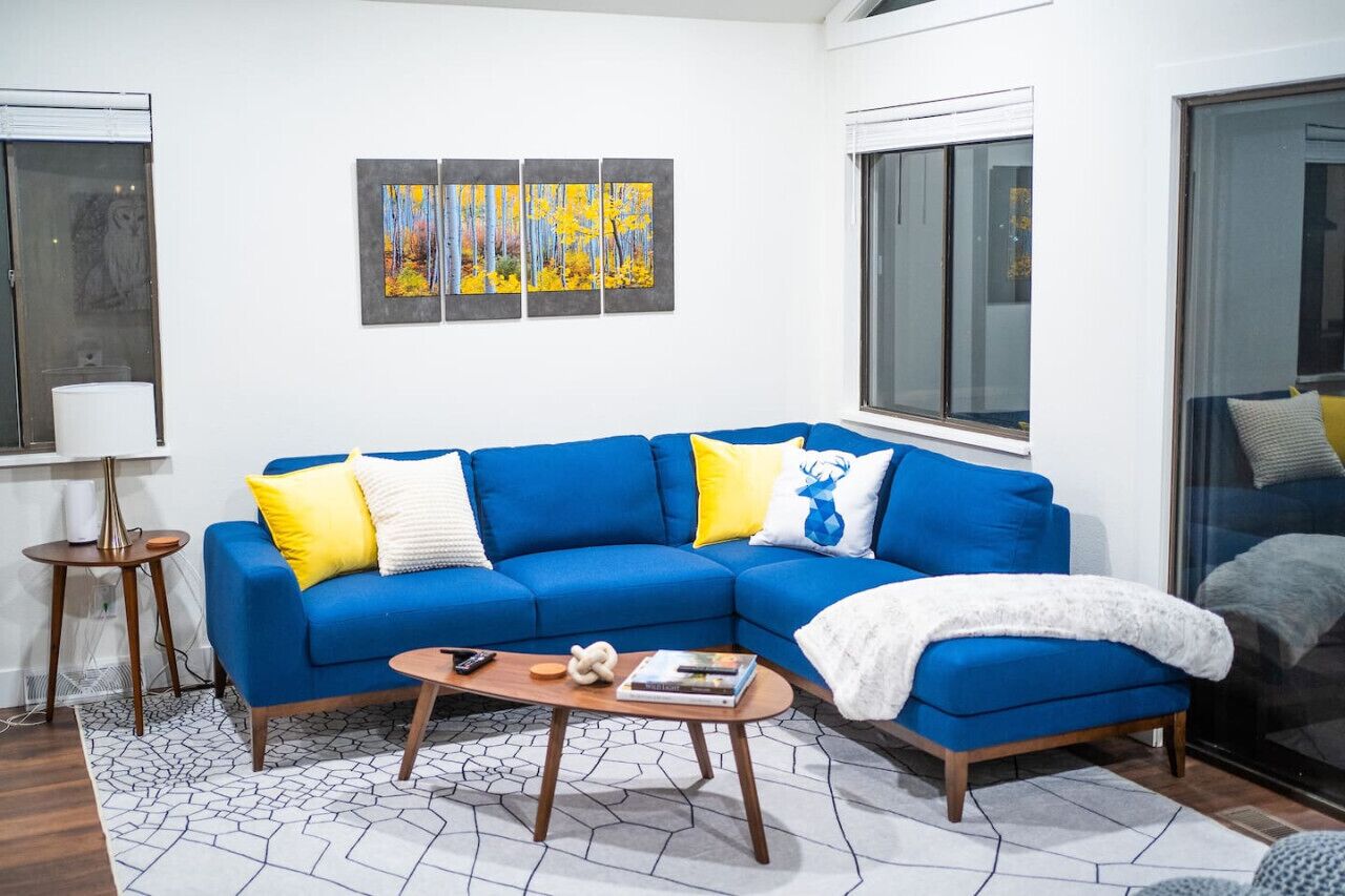 A modern living room with a blue sectional sofa, a coffee table, and a painting above the sofa.