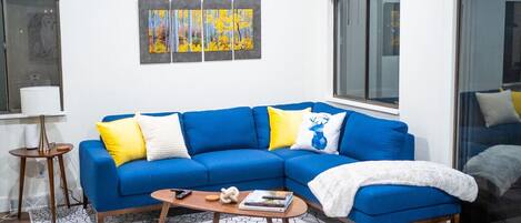 A modern living room with a blue sectional sofa, a coffee table, and a painting above the sofa.