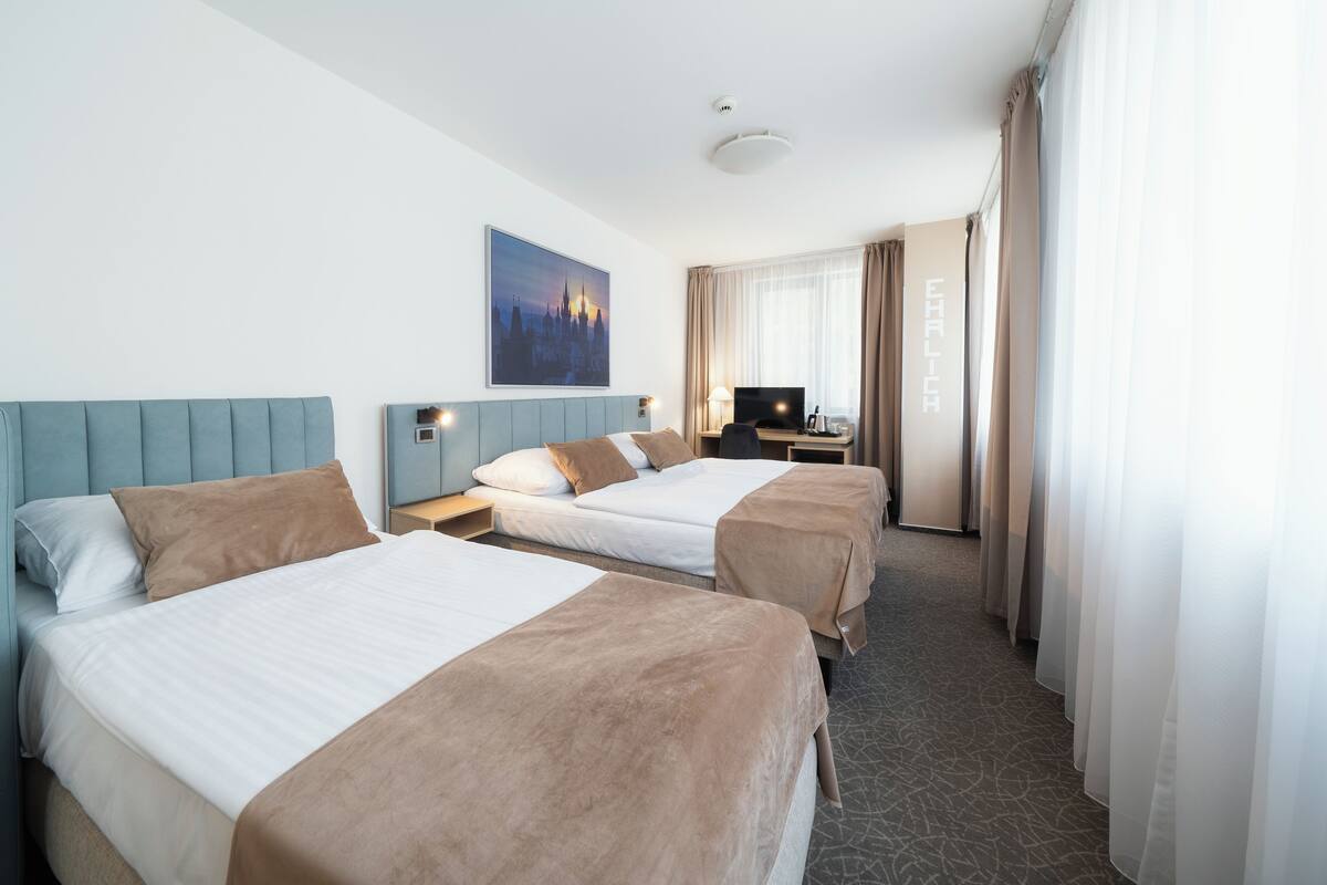 A hotel room with two beds, a TV, a desk, and a painting on the wall.