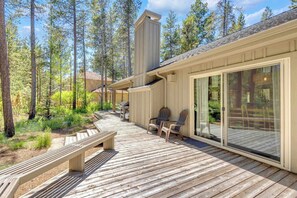 Eine Holzterrasse mit einer Bank, Stühlen, einem Grill und einem gläsernen Raum mit Schiebetüren.