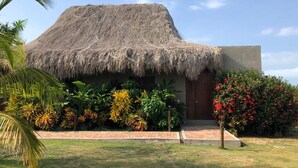 A thatched-roof building with a paved entrance, surrounded by tropical plants and a palm tree. - TERRITORIO MAGICO (Dibulla)