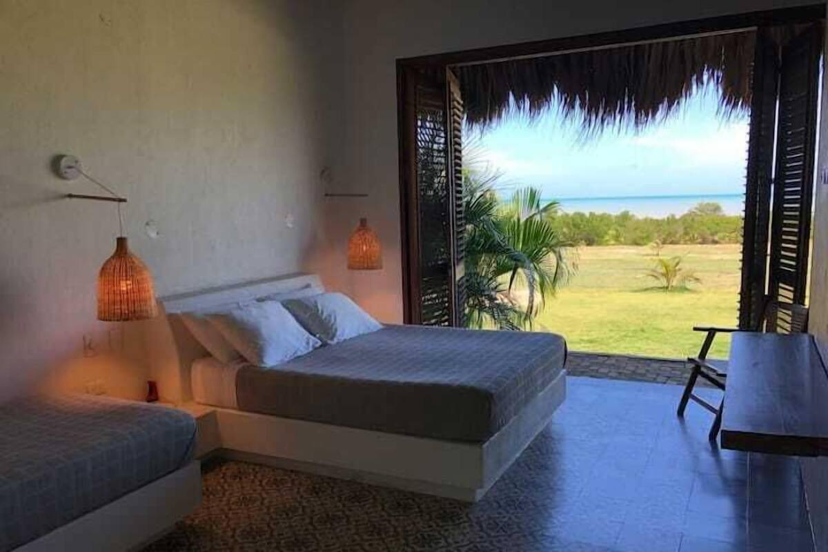 A bedroom with a bed, two bedside lamps, a view of the outdoors, and a small table.
