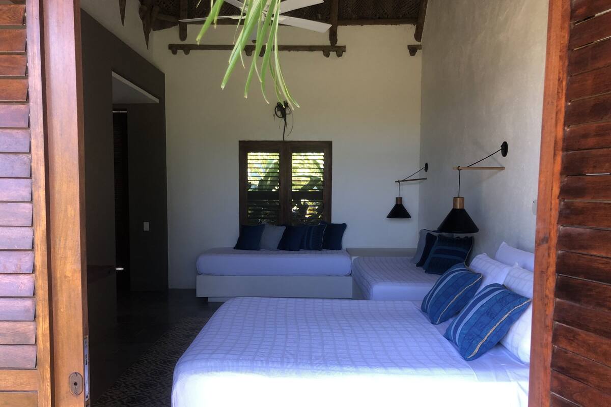 A bedroom with two beds, a window with blinds, and a ceiling fan.