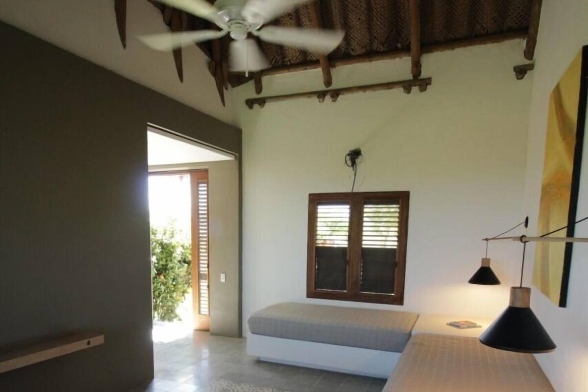 A bedroom with a bed, a ceiling fan, a window with blinds, and a bedside lamp.