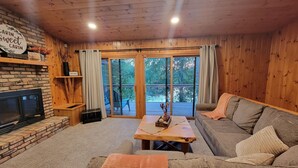 A cabin interior with a fireplace, a sofa, a coffee table, and a sliding glass door leading to an outdoor deck. - Family Cabin with hot tub on Cross lake (Crosslake)