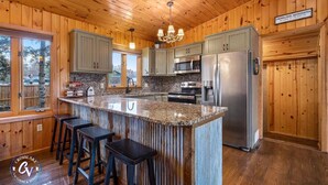 A wooden cabin kitchen with a granite island, bar stools, a refrigerator, and a sign indicating the location in Crosslake, Minnesota. - Family Cabin with hot tub on Cross lake (Crosslake)