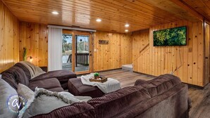 A wooden interior with a sofa, a television, and a sliding glass door leading outside. - Family Cabin with hot tub on Cross lake (Crosslake)