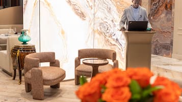 Eine Lobby mit zwei Sesseln, einem kleinen runden Tisch, einer dekorativen Vase und einem Mann, der einen Laptop an einem Podest benutzt.