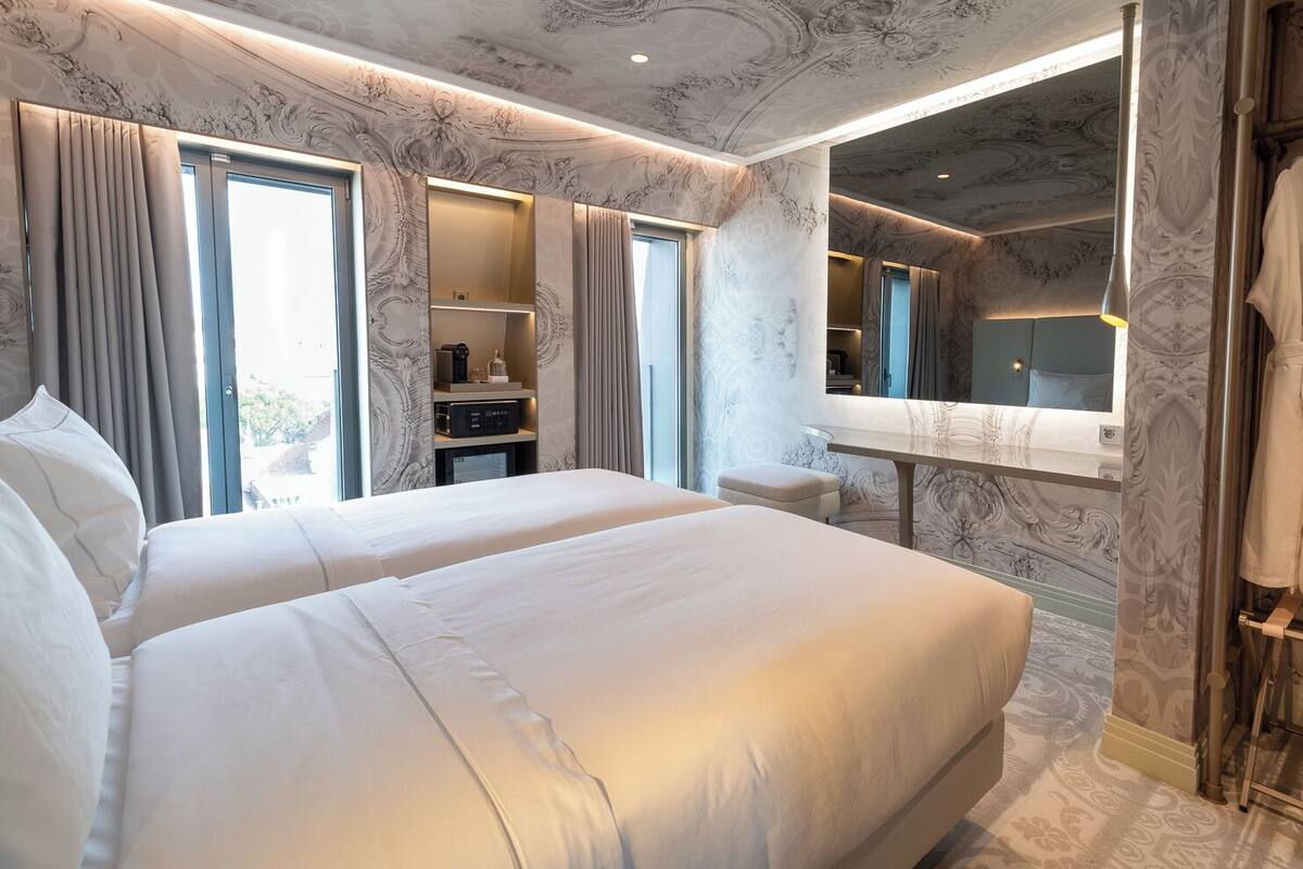 A hotel room with two beds, a vanity with a mirror, a robe rack, and a built-in desk.