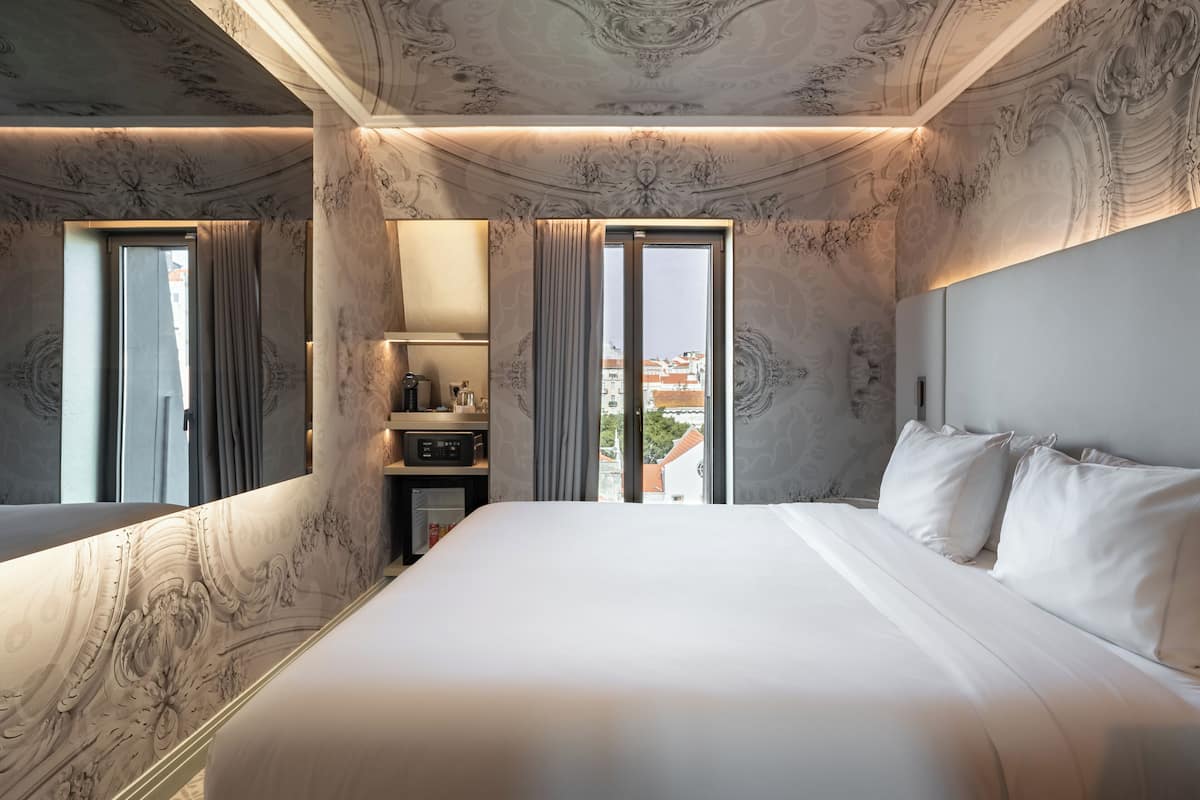 A hotel room with a large bed, a dresser, a mirror, and a view of the city.