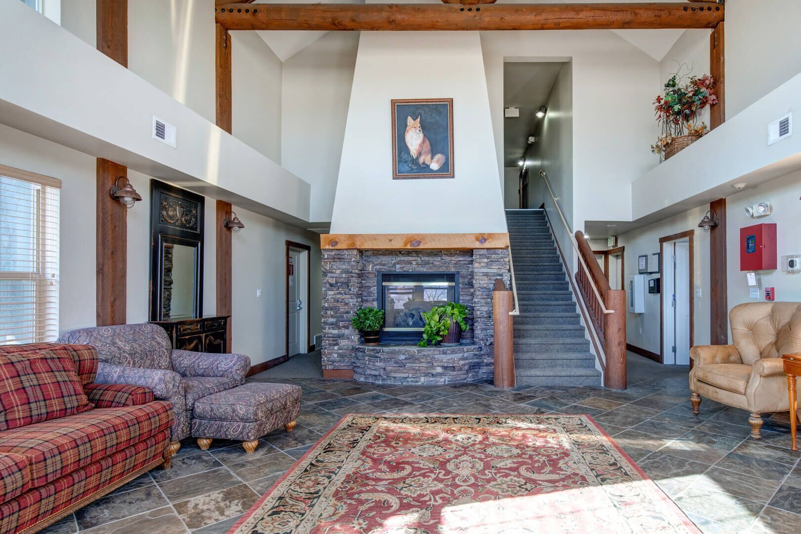 A spacious living area with a stone fireplace, a staircase, and a large window.
