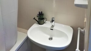 Uma casa de banho com uma pia branca, um espelho redondo, cortina de chuveiro e uma pequena planta em vaso.