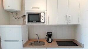 Uma cozinha compacta com armários brancos, micro-ondas embutido, cafeteira e pia de aço inoxidável.