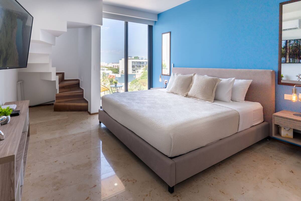 Una habitación de hotel moderna con una cama grande, un escritorio, un televisor y una escalera que lleva a un balcón.