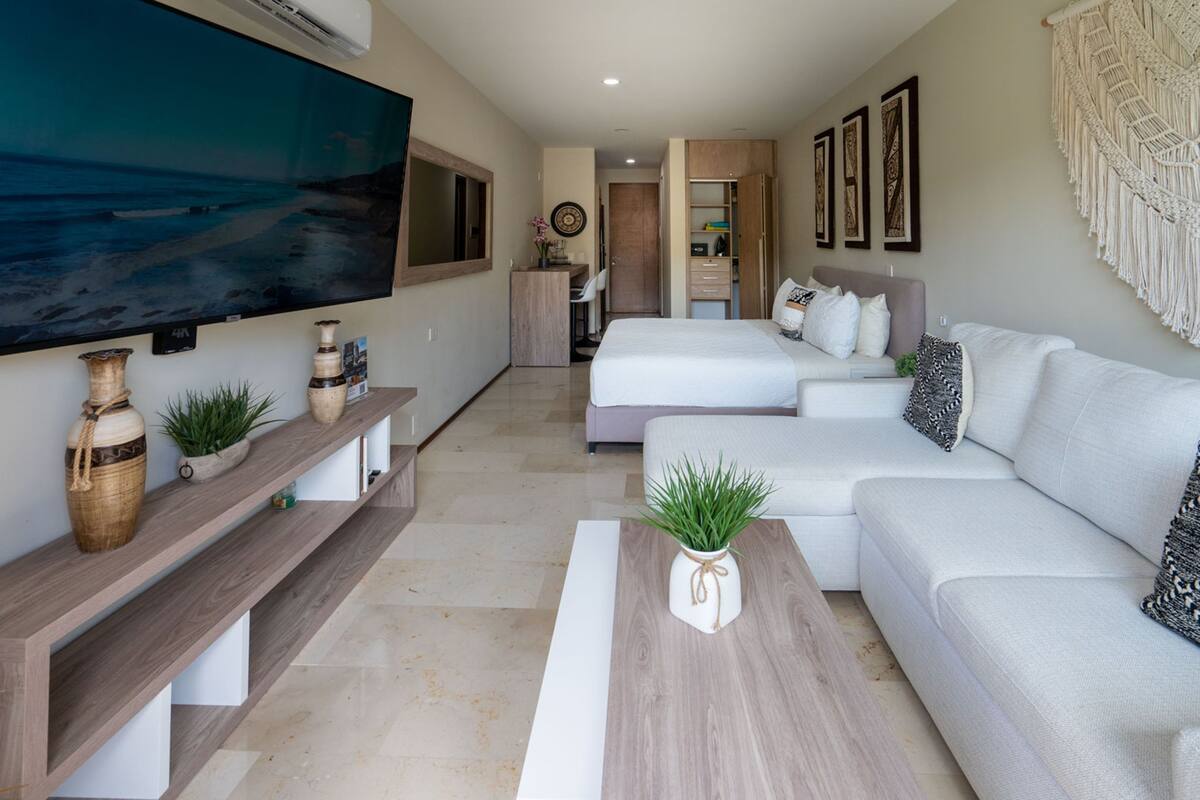 Una sala de estar moderna con un televisor de pantalla plana grande, un sofá, una cama y una mesa de centro con objetos decorativos.