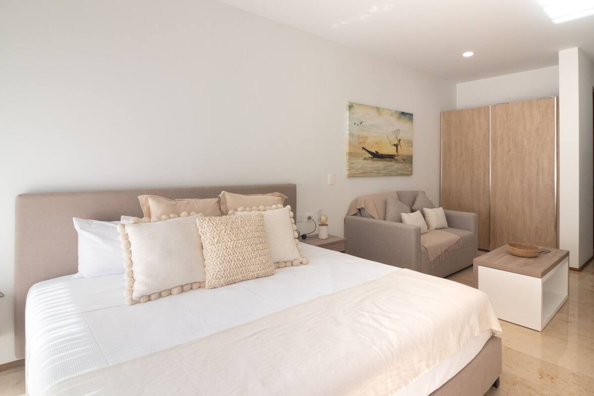 Un dormitorio moderno con una cama grande, un sofá, un armario de madera y un cuadro en la pared.