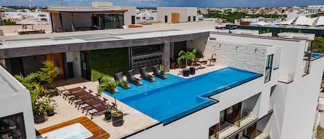 Área de piscina en la azotea con sillones de descanso, una bañera de hidromasaje y un bar.