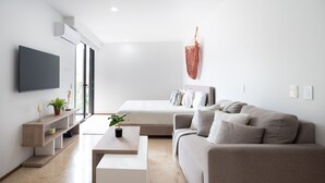 A modern, minimalist bedroom with a bed, a sofa, a TV, and a plant. - Perfect Place (Playa del Carmen)