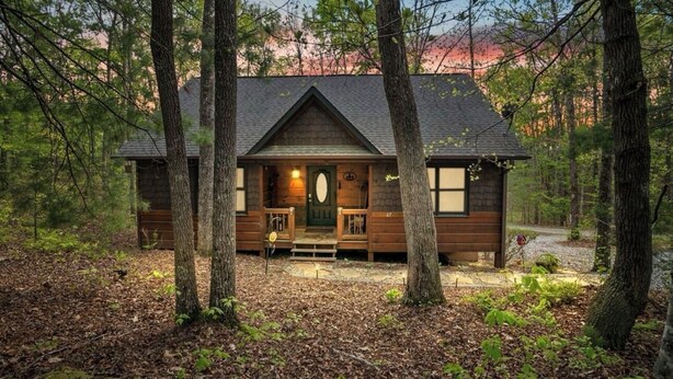 Une cabane dotée d’un porche à l’avant, d’une façade en bois et d’une porte avec un panneau de verre.
