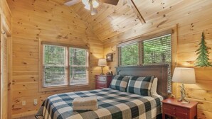 Une chambre dans un chalet en rondins, avec une couvre-lit à carreaux, deux lampes de chevet et une petite décoration en forme d’arbre accrochée au mur.