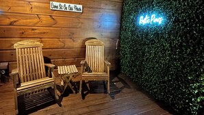 Une terrasse en bois avec deux chaises en bois et une petite table, un panneau lumineux au néon indiquant « Rustic Pines », et un panneau qui dit « Venez vous asseoir sur notre véranda ».