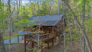 Une cabane dotée d’une terrasse et d’un petit porche, entourée d’arbres.