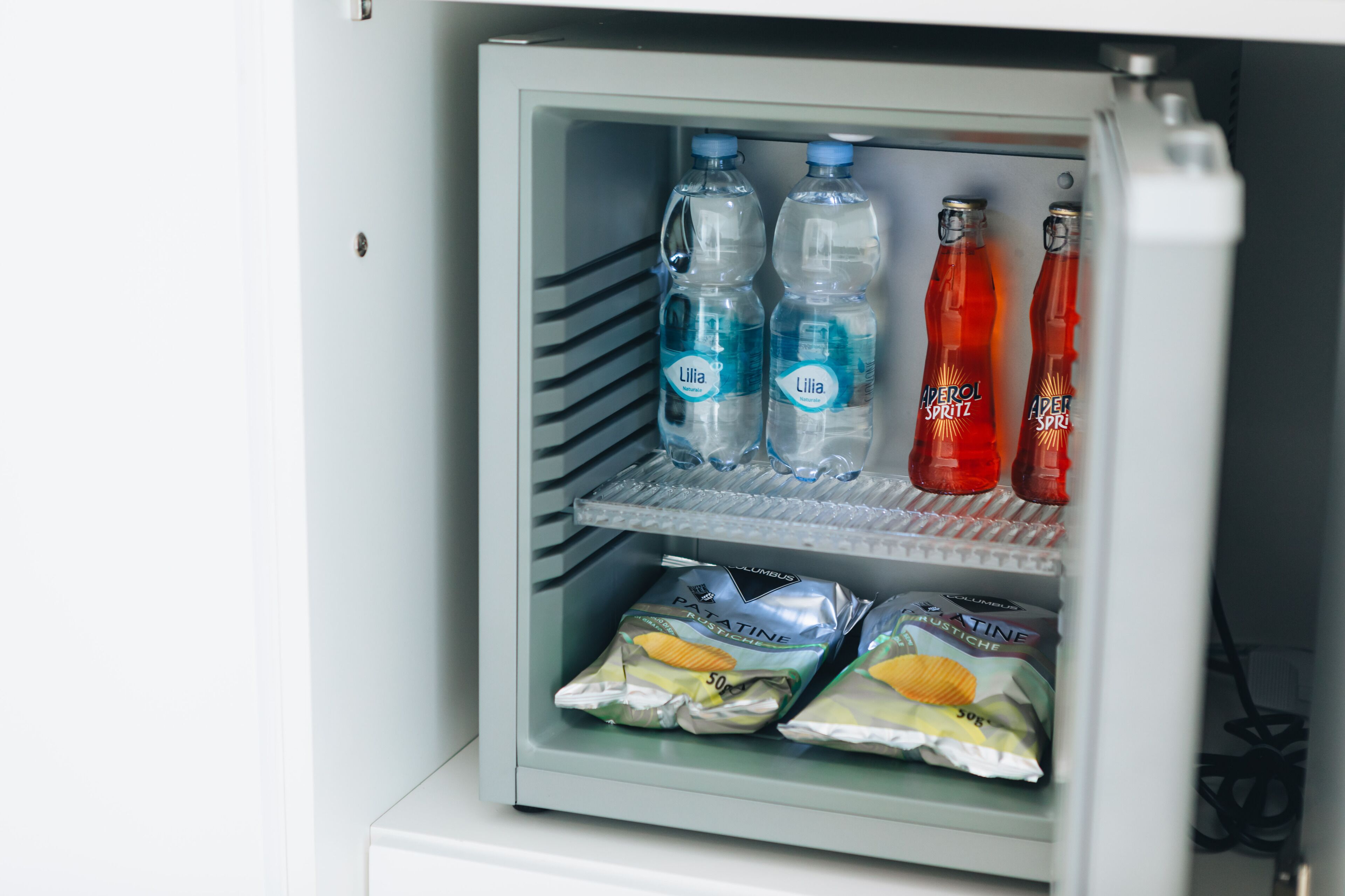 Mini-geladeira com garrafas de água, refrigerantes e embalagens de lanches.