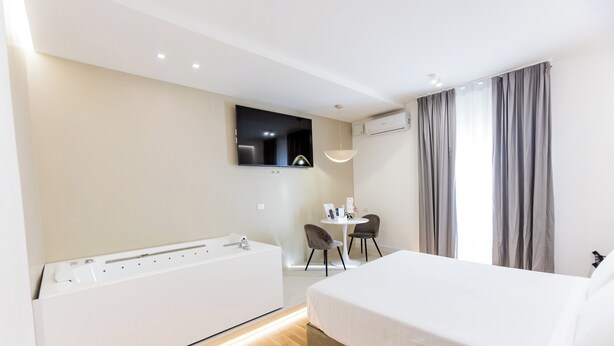 Een hotelkamer met een groot bed, een ingebouwd bad, een klein tafeltje met stoelen, een aan de muur bevestigde televisie en een airconditioning.